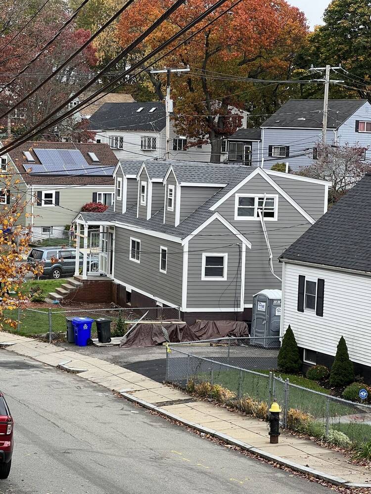 Finished Cape with three dormers and gray siding, seen from up the street