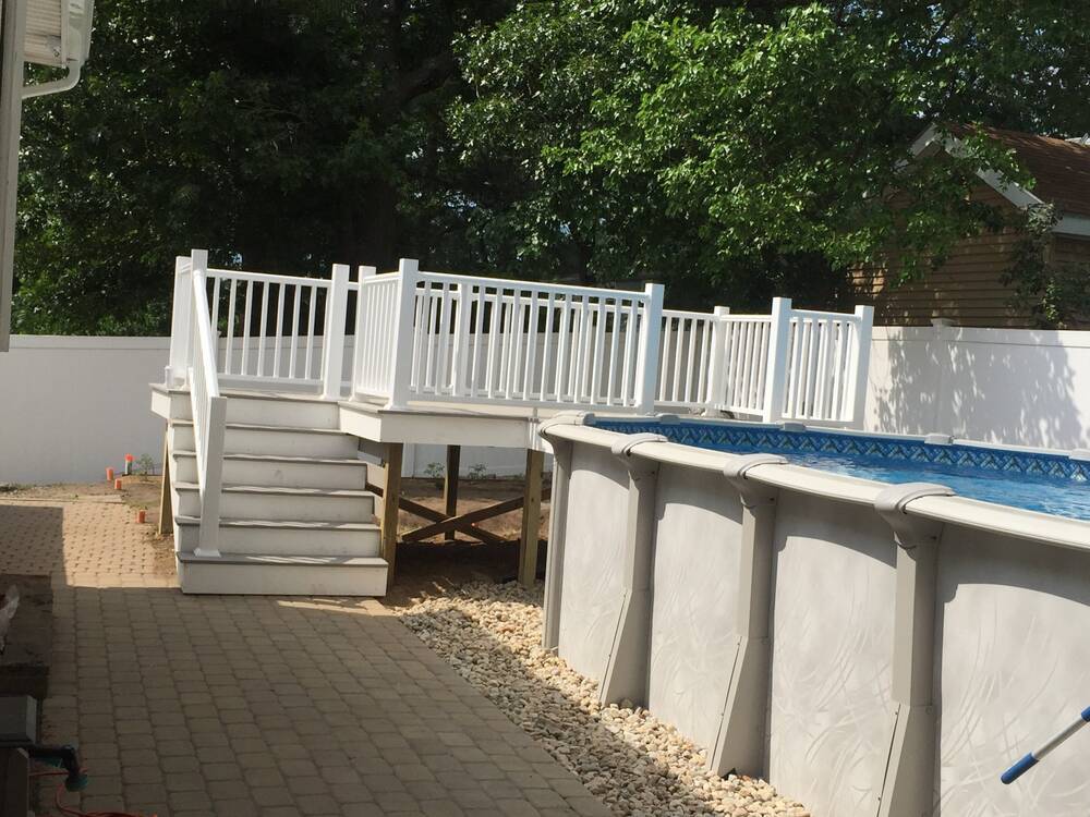 Raised composite pool deck with white vinyl railings and stairs to the patio