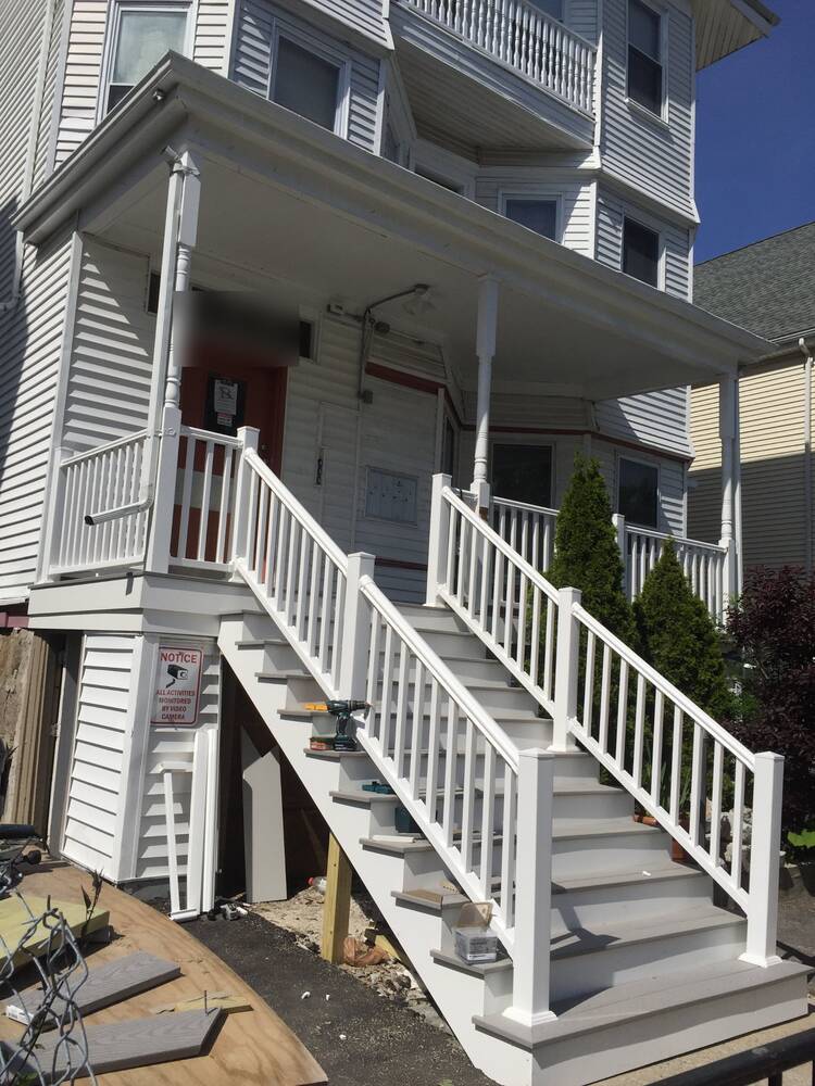 New front stairs with white vinyl railings being installed on a triple-decker