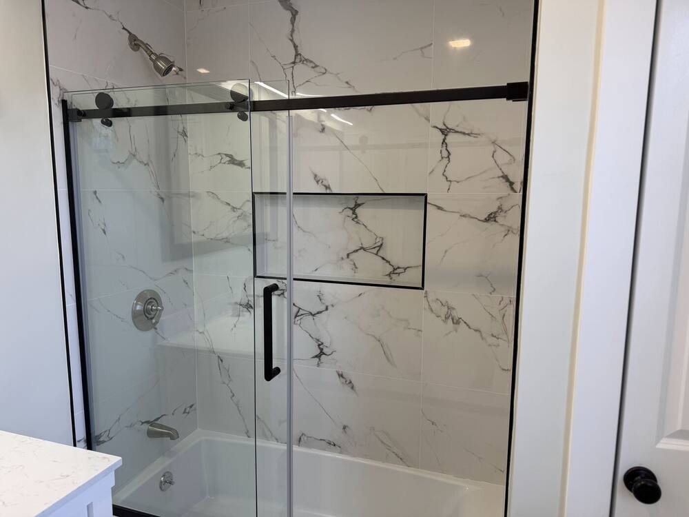 Marble-look shower with black-framed sliding glass door and niche