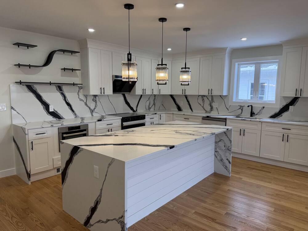 White shaker kitchen with a black-veined quartz waterfall island, slab backsplash and glass pendants