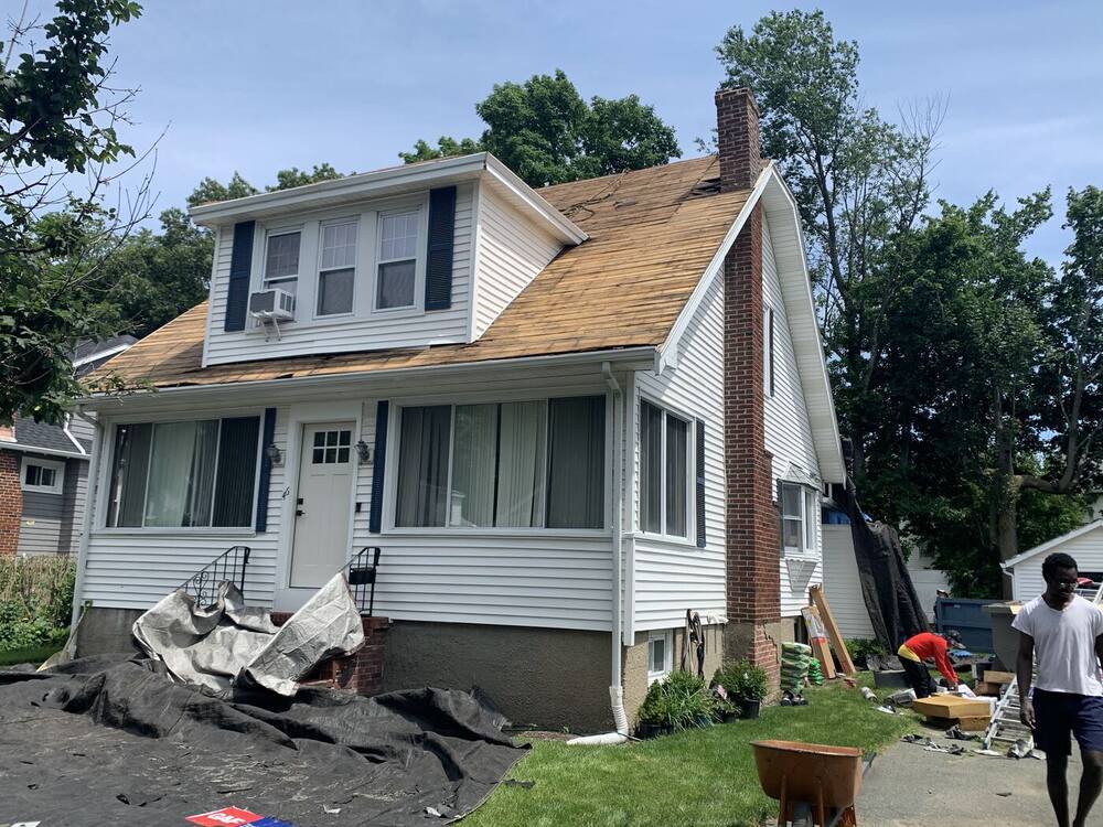 Old roofing stripped down to the boards on a bungalow, with tarps protecting the yard