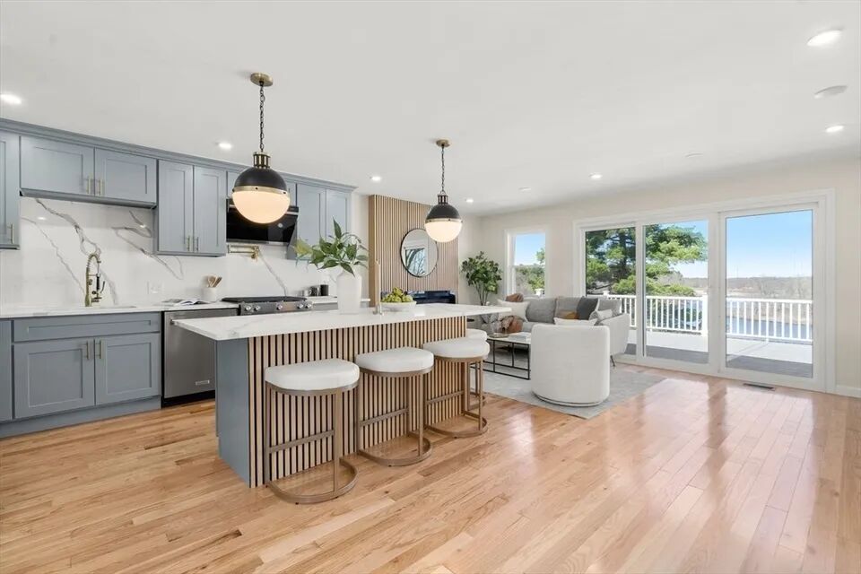 Open kitchen and living room in a Dedham whole-house renovation, with a slatted wood island, brass globe pendants and deck view