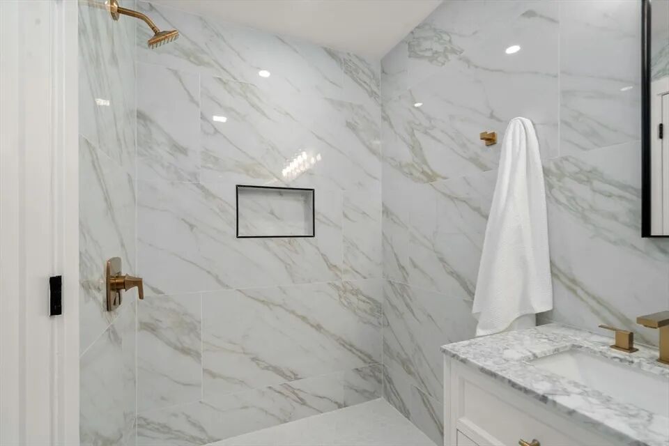 Curbless marble-look shower with brass fixtures and a black-framed niche